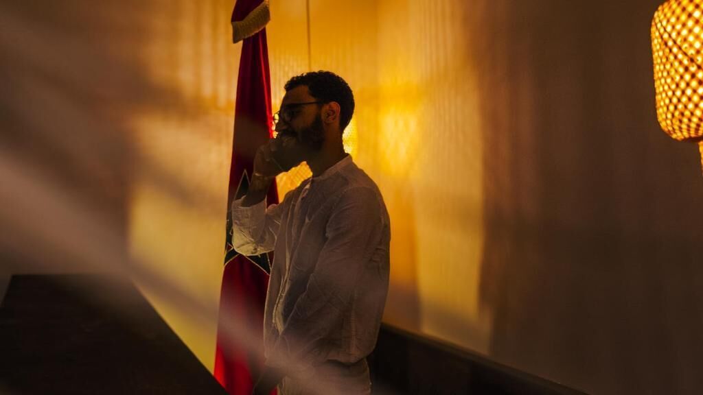 A person standing in a corridor with a red flag, a wall with a textured pattern, and a light fixture.