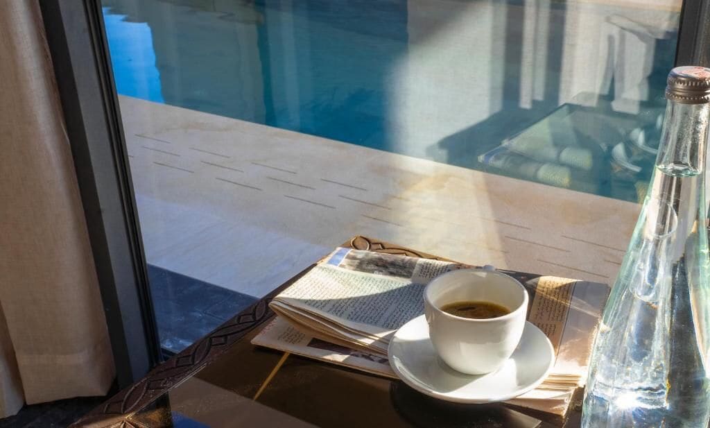 A table with a cup of coffee, a newspaper, and a bottle.