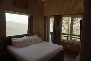 Ein Schlafzimmer mit einem großen Bett, Holzwänden, einem Fenster mit Blick ins Freie und einem Balkon.
