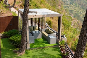 A covered outdoor seating area with wicker furniture and a view of a hilly landscape.