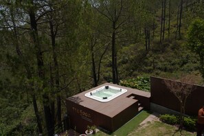 A modern outdoor hot tub area with a wooden deck, surrounded by dense forest.