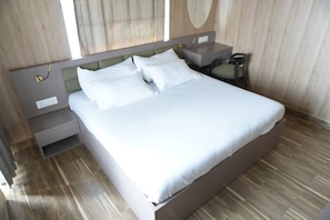 A neatly made bed with white linens, a wooden headboard, a nightstand with a lamp, and a chair.