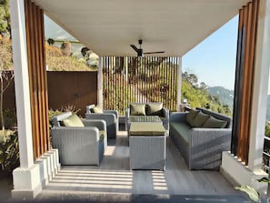 An outdoor seating area with wicker furniture and a ceiling fan, overlooking a scenic landscape.