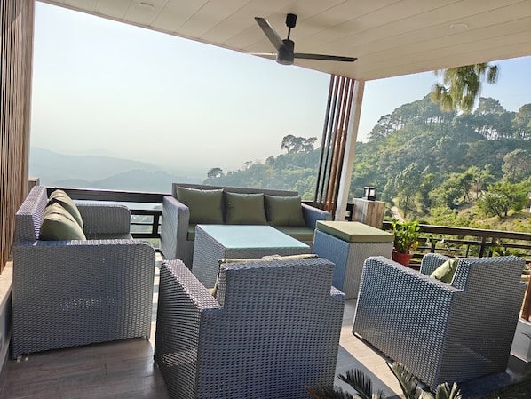 A balcony with wicker furniture, a ceiling fan, and a view of a mountainous landscape.