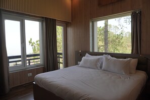 A bedroom with a large bed, two windows, and a view of trees.