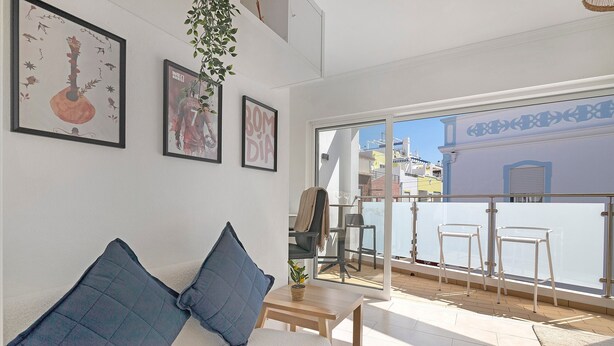Ein modernes Wohnzimmer mit einer Couch, einem kleinen Tisch und einem Balkon mit Stühlen.