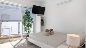 Ein modernes Schlafzimmer mit einem Bett, einer Nachttischlampe, einem an der Wand montierten Fernseher, einem Topfpflanzen und Blick durch eine Schiebetür.