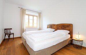Ein Doppelbett mit Holz Kopfteil, ein Sessel, ein Fenster mit Vorhängen und eine Nachttischlampe.