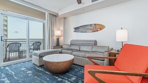 Een moderne hotelkamer met balkon, een grijze bank, een ronde salontafel en een feloranje fauteuil.