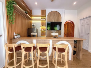 A kitchen with wooden paneling, a central island with bar stools, a refrigerator, a television, and a wooden door.
