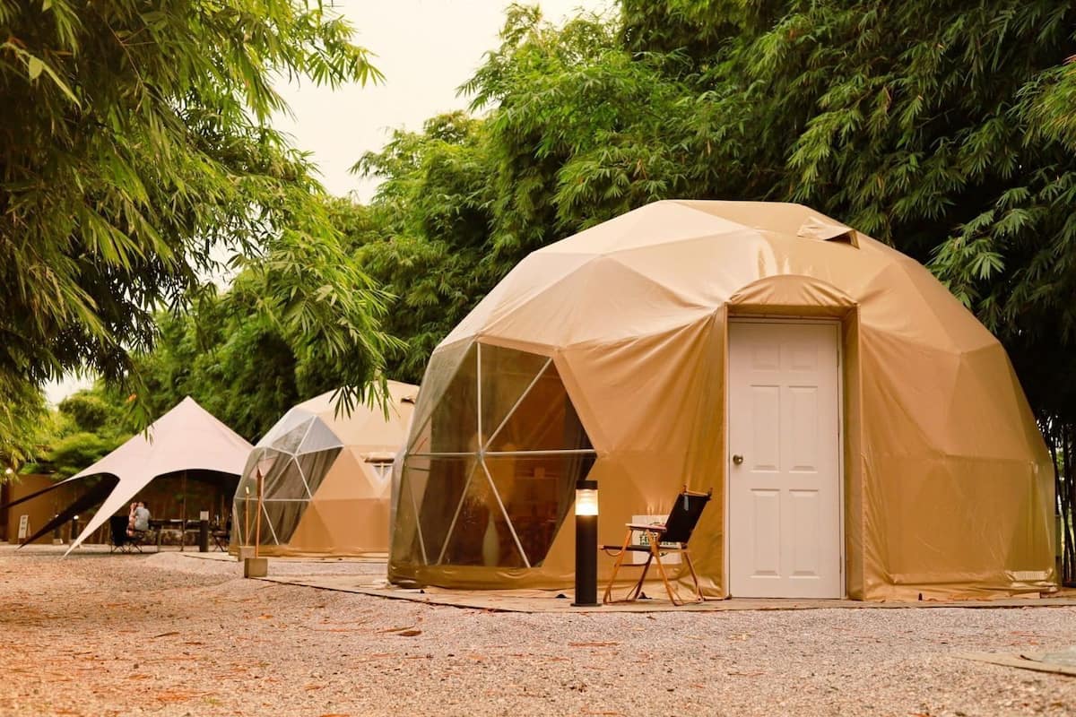 A series of dome-shaped tents with a door and a small table outside, surrounded by trees.