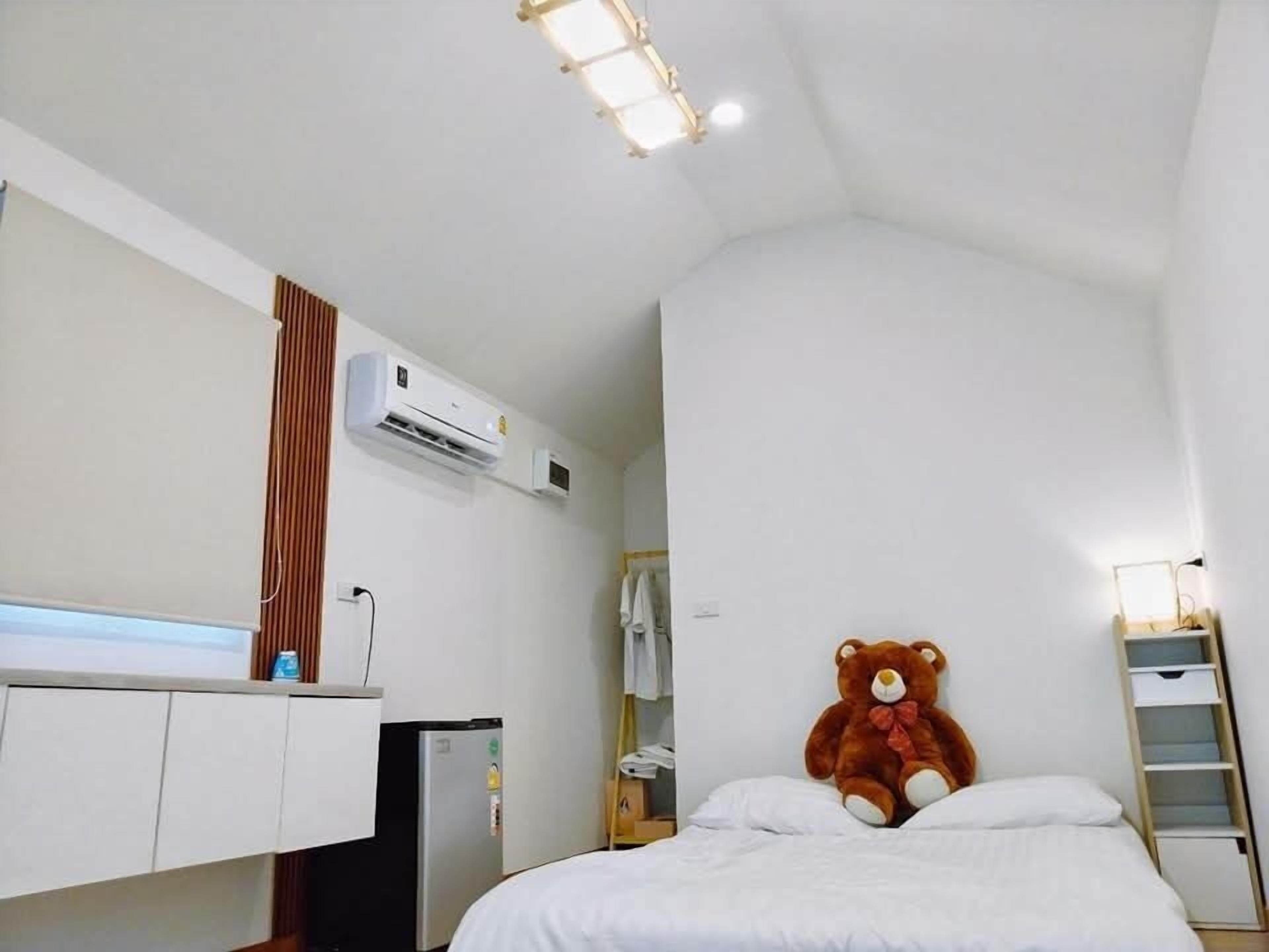 Un dormitorio con cama, un oso de peluche, un armario, un escritorio, una silla y un equipo de aire acondicionado.
