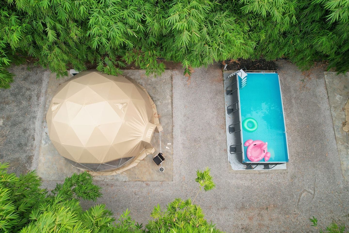 Una estructura en forma de tienda geométrica junto a una piscina rectangular con un dispositivo de flotación rosado.