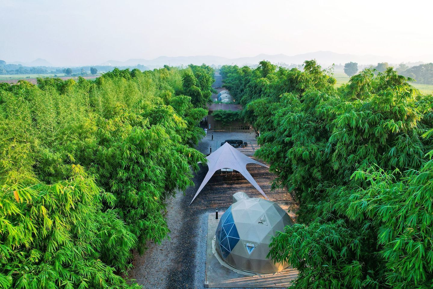 A pathway leading through a lush green garden with a geometric structure and a dome-shaped building.