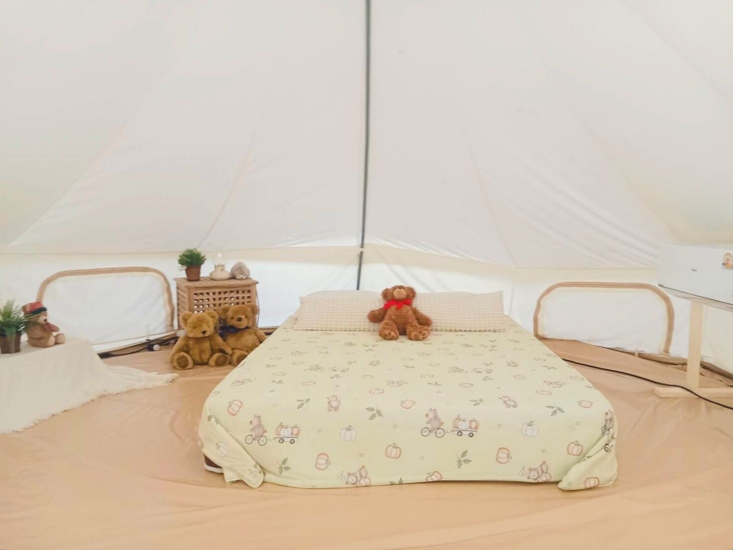 A tent with a bed, two teddy bears, a small table with a plant, and a lamp.