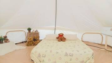 A tent with a bed, two teddy bears, a small table with a plant, and a lamp.
