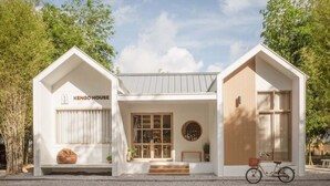 Ett modernt, vitt KENGO-HUS med en trädörr, en cykel och en bänk utanför.