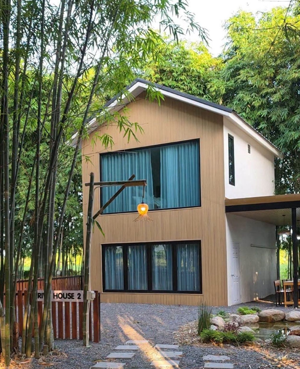 A modern two-story house with a covered porch, surrounded by bamboo and a small garden.