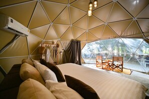 A tented accommodation with a bed, pillows, a table, chairs, and an air conditioning unit.