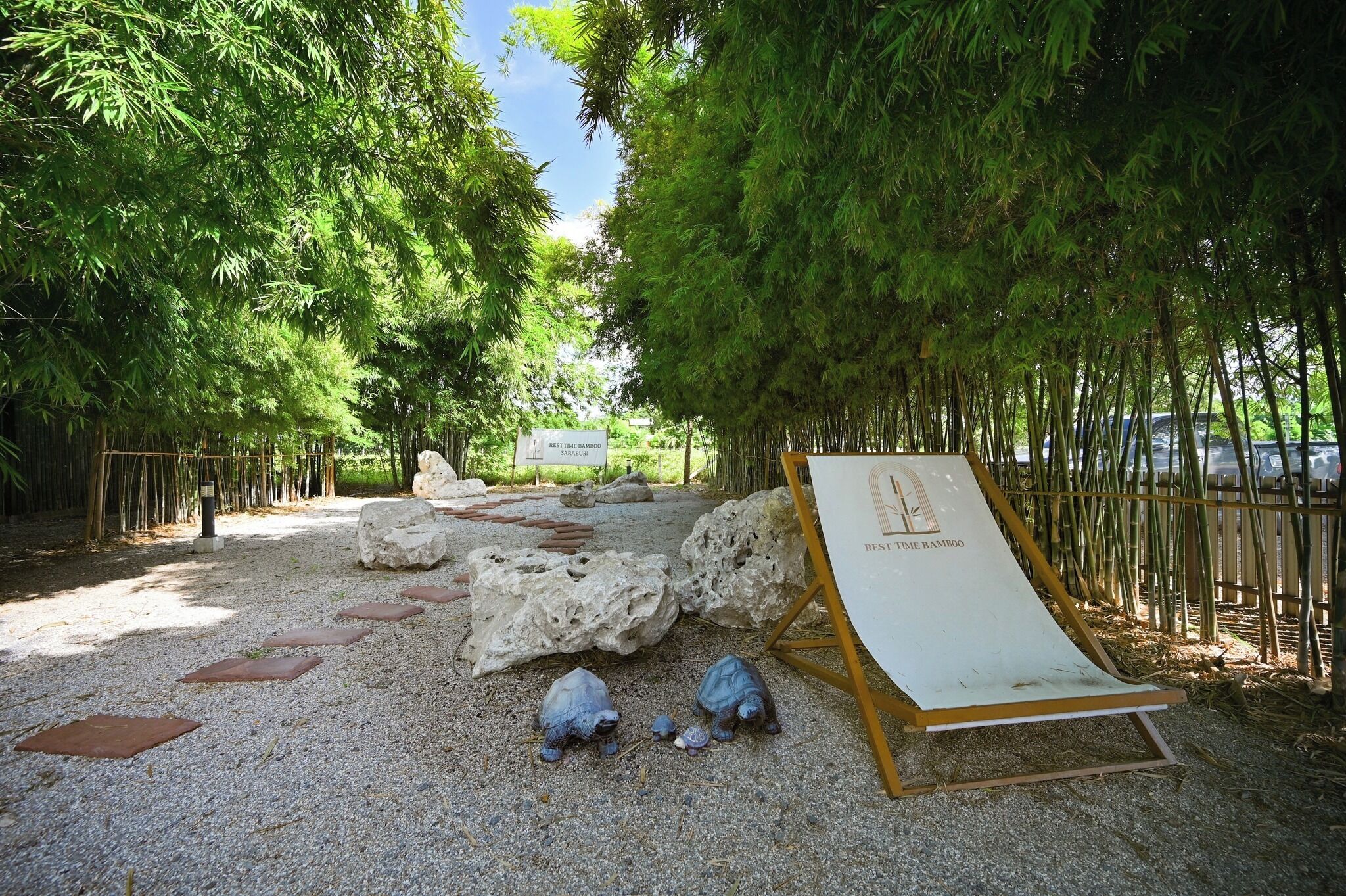 Un sendero bordeado de rocas y bambú, que lleva a una zona de estar con un cartel que dice 'REST THE BAMBOO'.