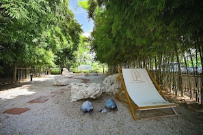 Un sendero bordeado de rocas y bambú, que lleva a una zona de estar con un cartel que dice 'REST THE BAMBOO'.