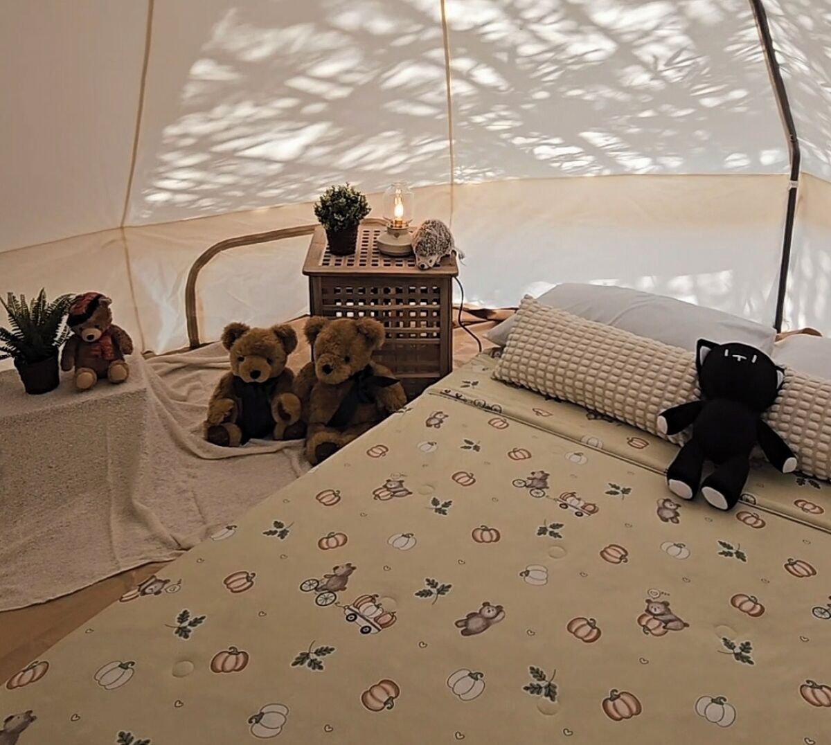 A tent with a bed, a small table with a lamp, and stuffed animals.