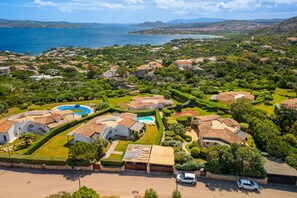 An aerial view of a residential area with houses, a swimming pool, and a view of the sea.