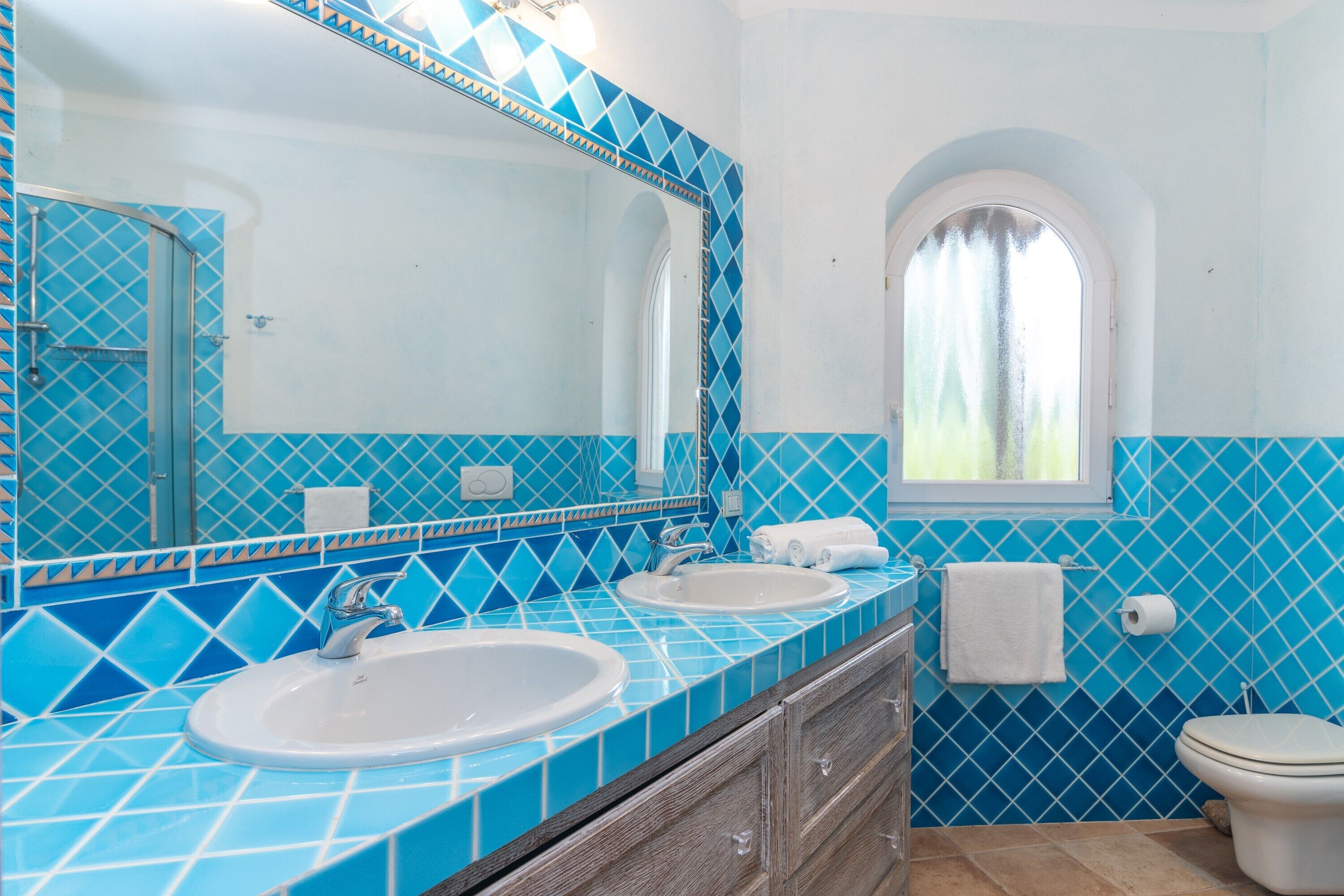 Une salle de bain avec deux lavabos, un miroir, une fenêtre et des toilettes.