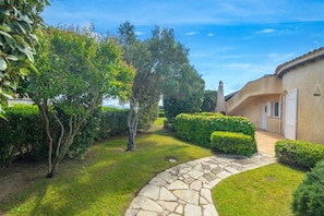 A well-maintained garden with a stone pathway leading to a building with a curved roof and white doors.