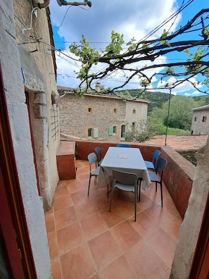 An outdoor patio with a table and chairs, stone buildings in the background, and a clear sky. - Authentic 13th-century Cévennes house (Thoiras-Corbès)