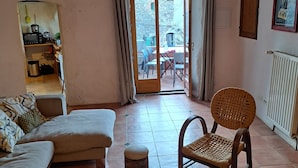 A living room with a sofa, chairs, a round table, a hanging light, and a view through a glass door to an outdoor area. - Authentic 13th-century Cévennes house (Thoiras-Corbès)