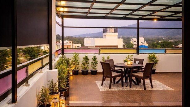 A rooftop terrace with a dining table and chairs, potted plants, and a view of the cityscape. - Hill View Comforts-Foot hills of Chamundi Hills. Pet-Friendly! (Mysuru)
