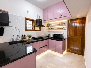 Eine moderne Küche mit schwarzen Arbeitsplatten, rosa Schränken und einer Holztür.