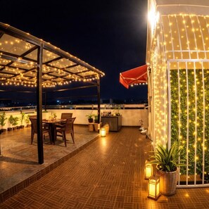 A rooftop terrace with a covered seating area, potted plants, and string lights.