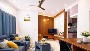 A modern living room with a sofa, coffee table, TV, and a dining area with a table and chairs. - Hill View Comforts-Foot hills of Chamundi Hills. Pet-Friendly! (Mysuru)