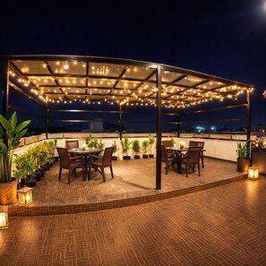 An outdoor patio with tables and chairs, string lights, and potted plants.