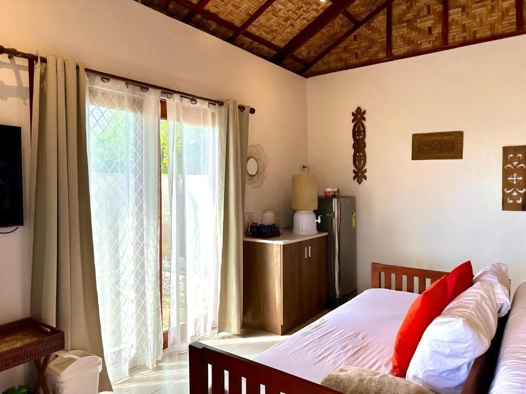 Un dormitorio con cama, cortinas, escritorio, refrigerador y decoración en la pared.