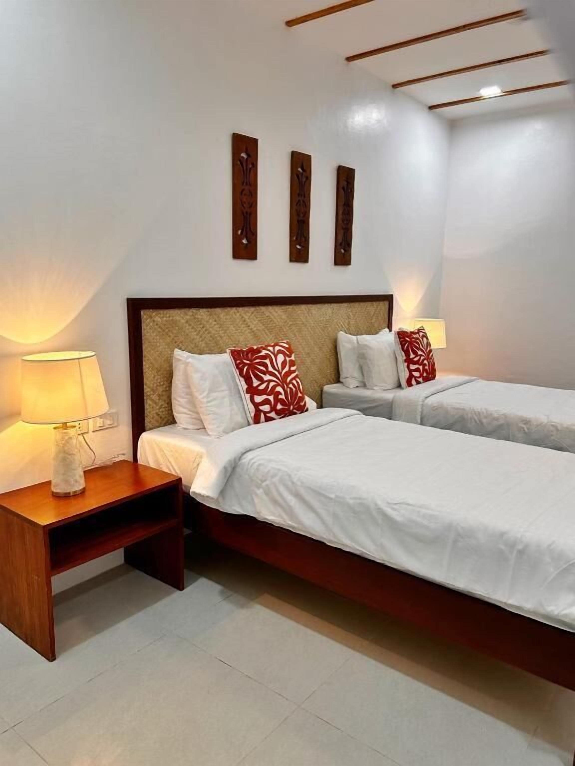 A hotel room with two beds, bedside lamps, a wooden headboard, and wall-mounted artwork.