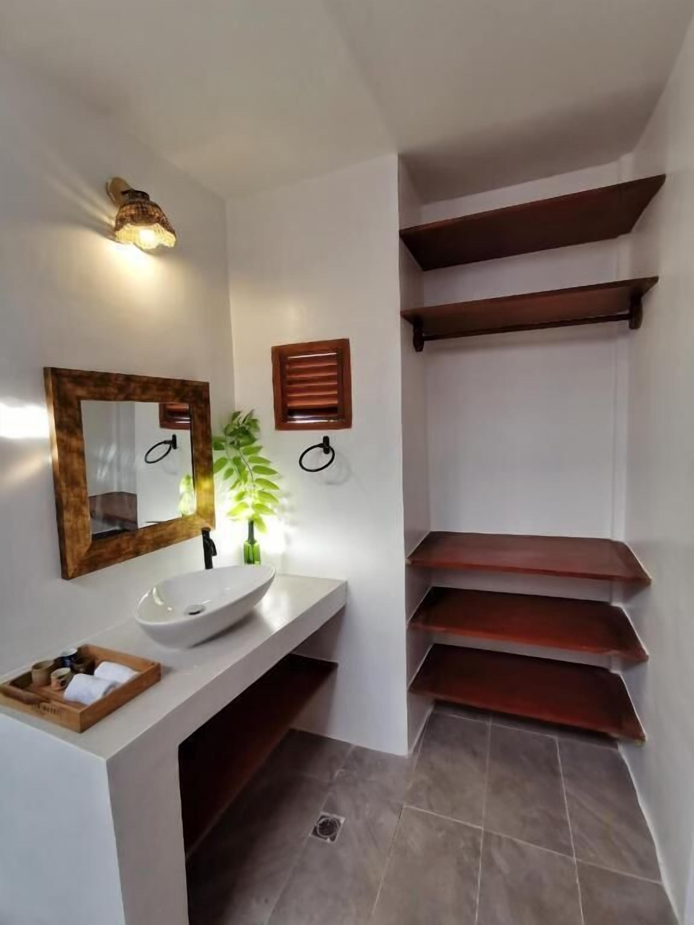 A modern bathroom with a white sink, mirror, and wooden shelves.