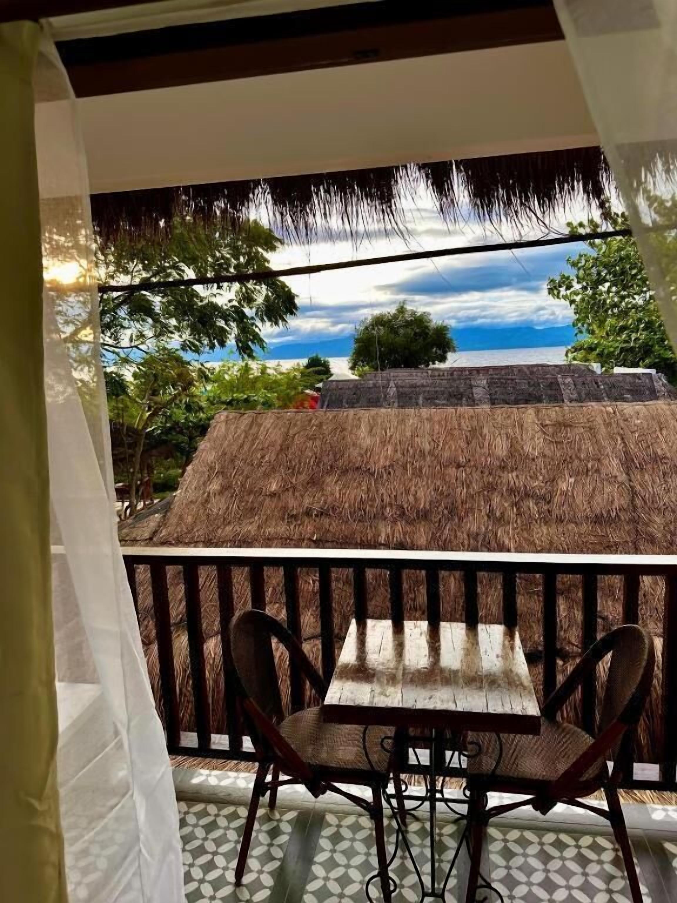 A balcony with a thatched roof, two chairs, and a table.