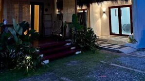 Un edificio de dos pisos con techo de paja, un balcón y una entrada bien iluminada.