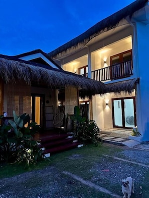 A two-story building with a thatched roof, a balcony, and a well-lit entrance. - Uzuri Kubo Huts & Kwartos (Moalboal)