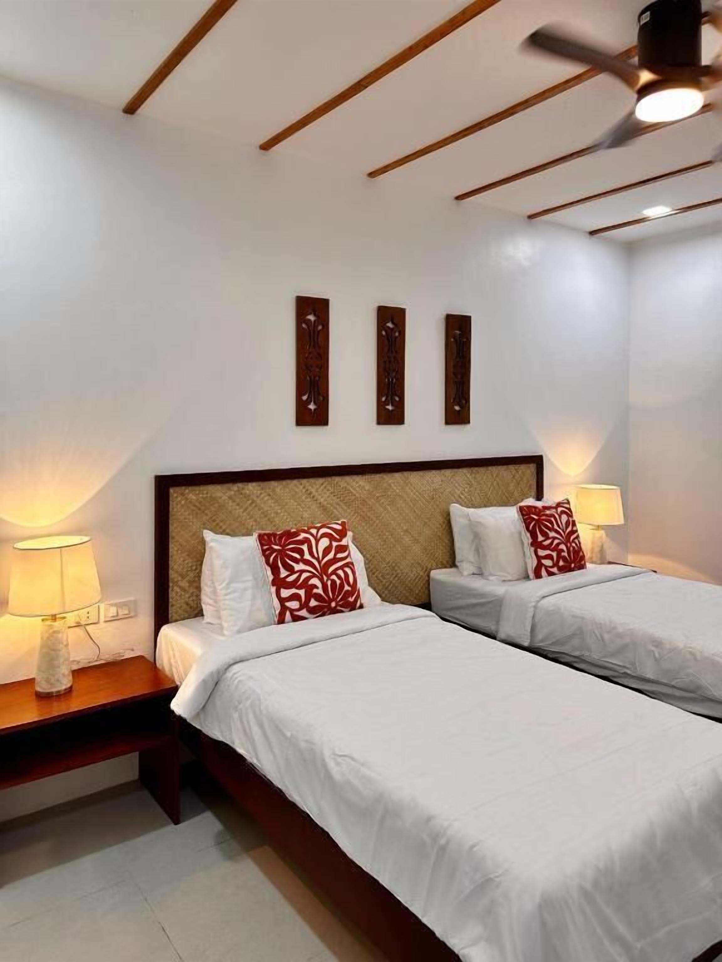A hotel room with two beds, a wooden headboard, bedside lamps, and a ceiling fan.