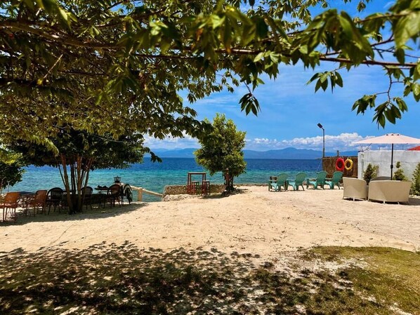 A beach with outdoor seating, a table, and chairs.