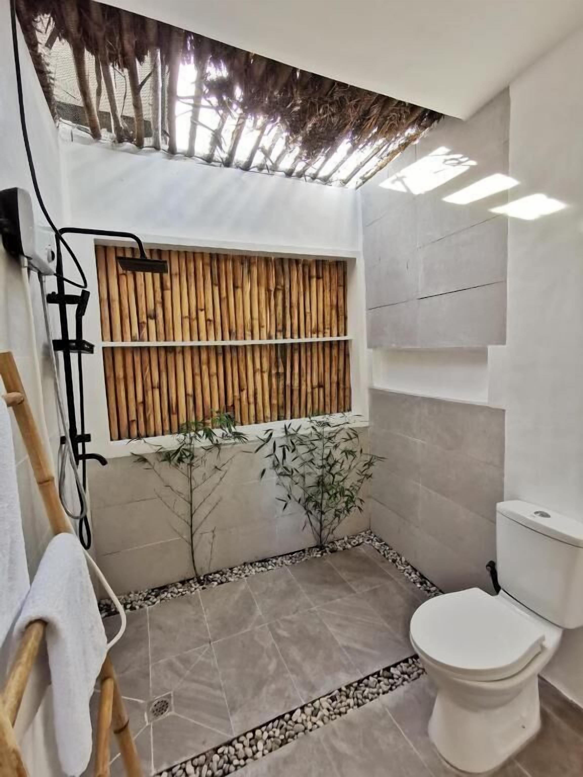 A bathroom with a toilet, a bamboo wall, and a tiled floor.