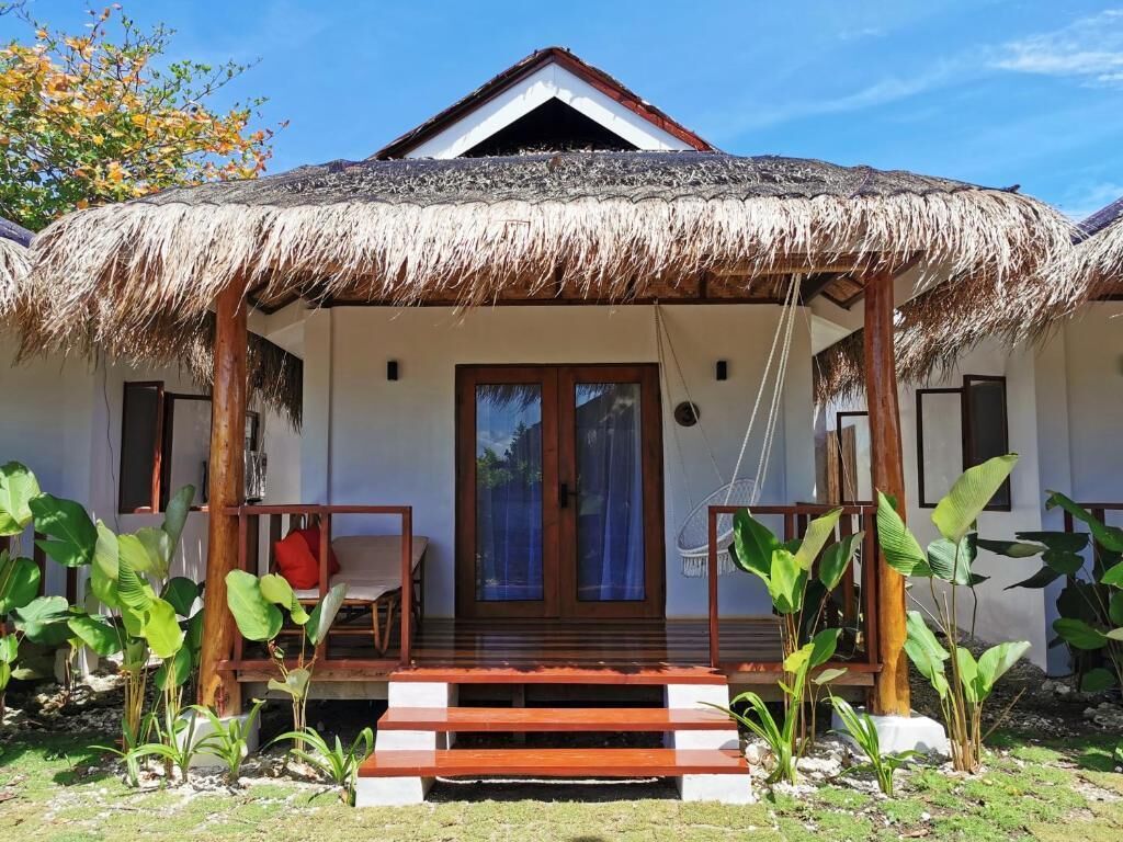 A bungalow with a thatched roof, wooden porch, and a small garden.