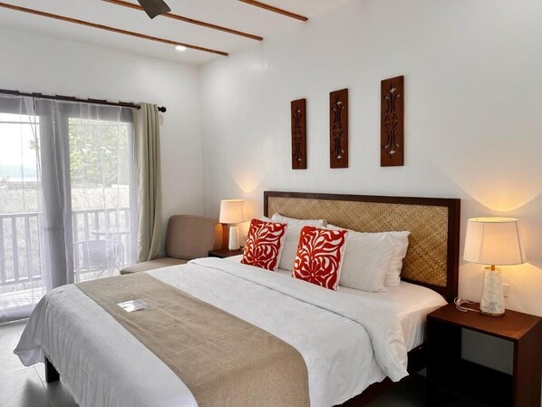 A hotel room with a bed, two bedside tables with lamps, a window with curtains, and three wall-mounted decorative panels.