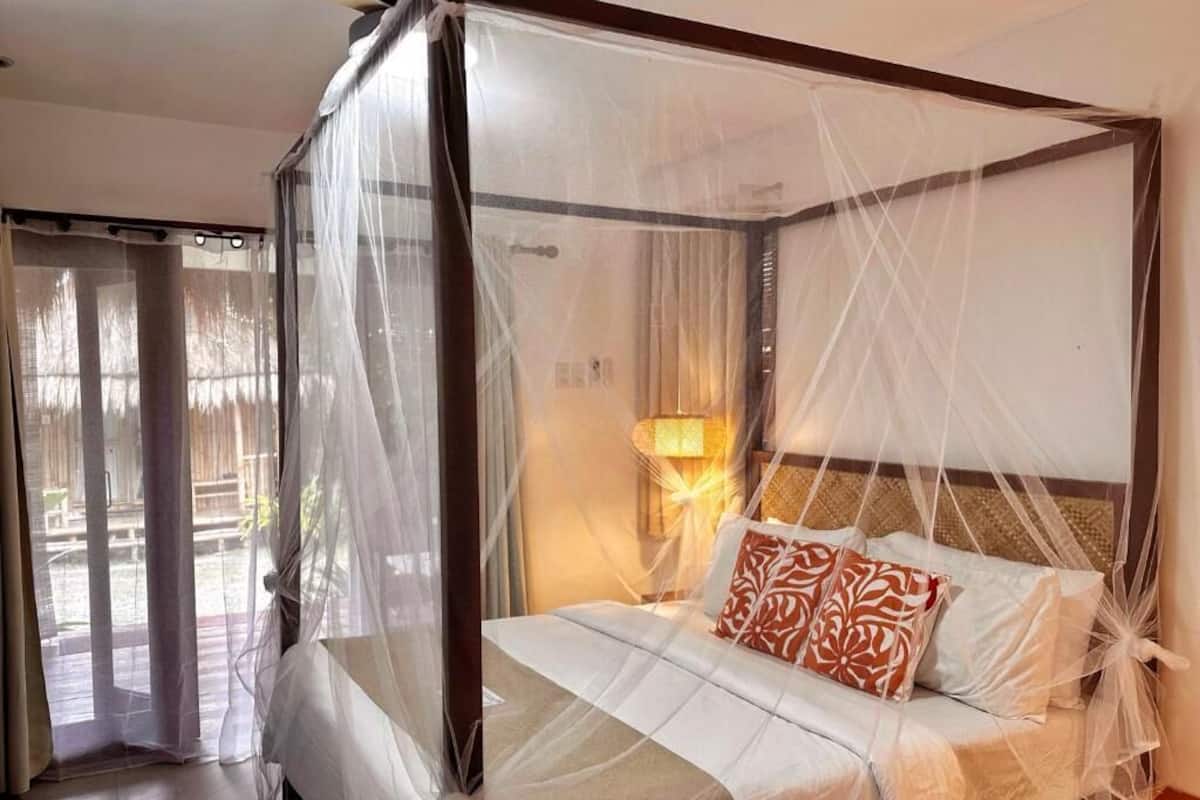 Una cama con dosel, una lámpara de noche y vistas a un espacio exterior a través de un ventanal.