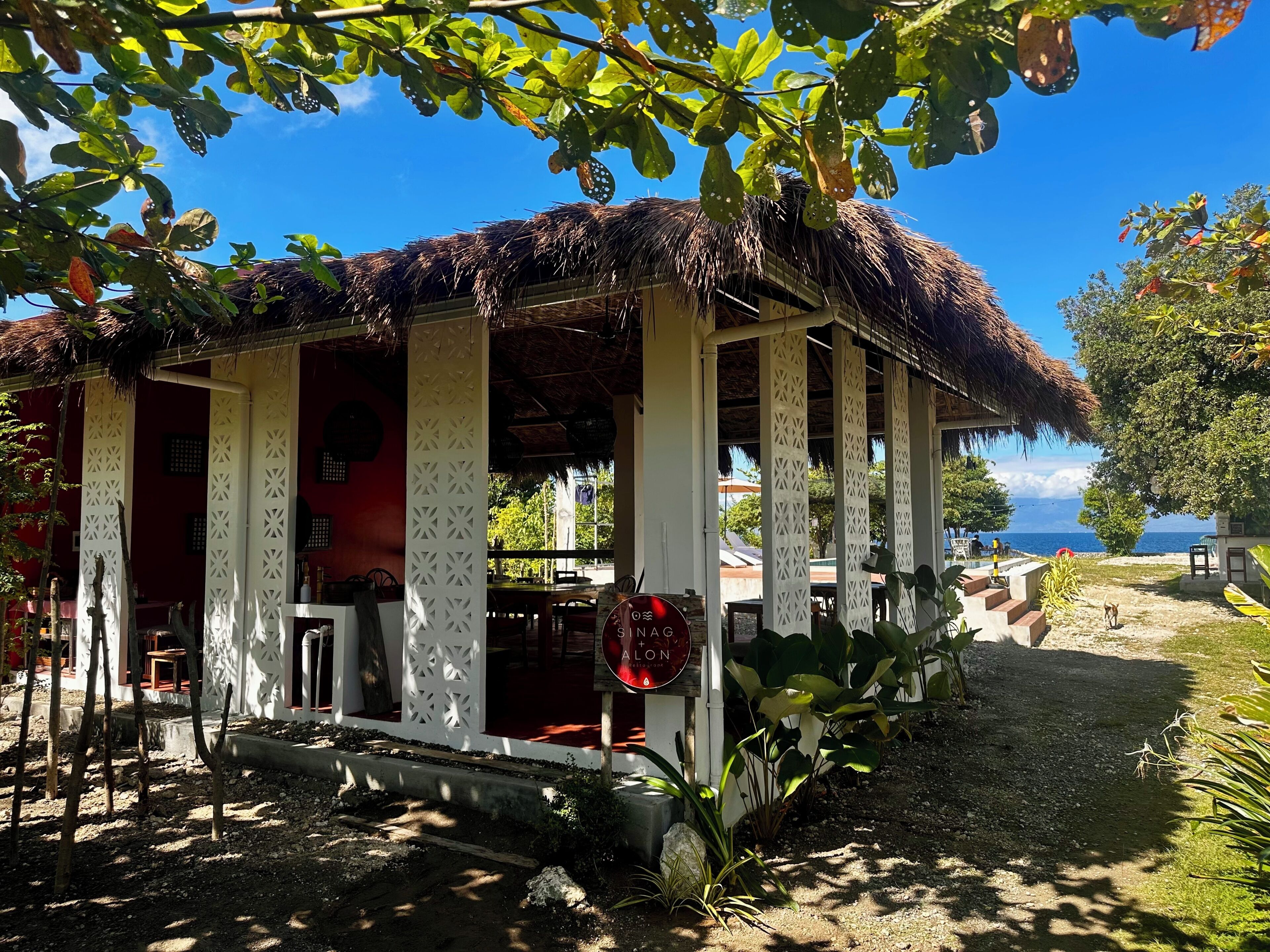 A thatched-roof structure with a white facade and a sign indicating 'Sana Lodge.'