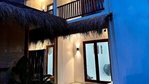 Un edificio de dos pisos con balcón, ventanas amplias y estructura de techo de paja.